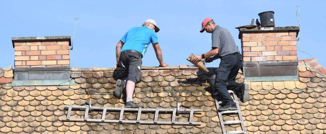 Dachdecker inspizieren einen Altbau: Schon mit vergleichsweise geringem Aufwand lässt sich die Klimabilanz stark verbessern.